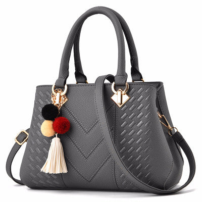 Chic gray luxury handbag for women, featuring a modern design with textured patterns and vibrant pom-pom decor.