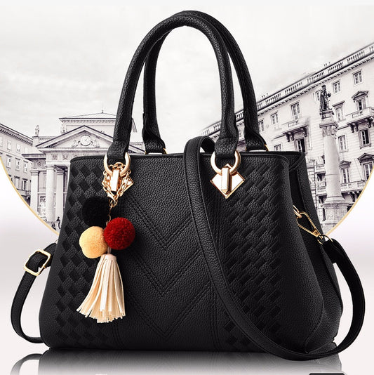 Stylish black luxury handbag for women featuring a textured design, gold accents, and a colorful pom-pom keychain.